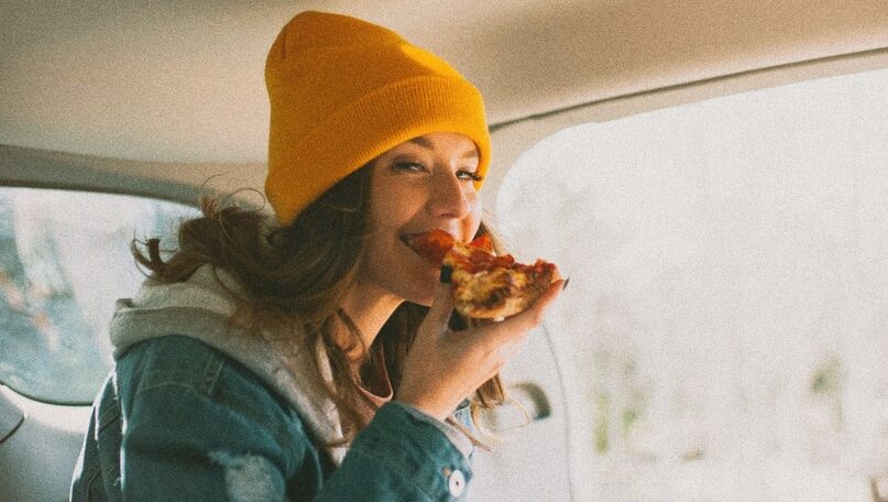 woman eating pizza inside vehicle